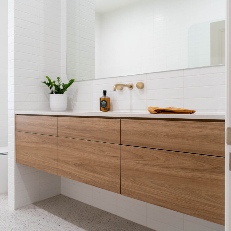 Beautiful bathroom longline drawer vanity in walnut and large rounded corner mirror. White light and bright with terrazzo tiles.