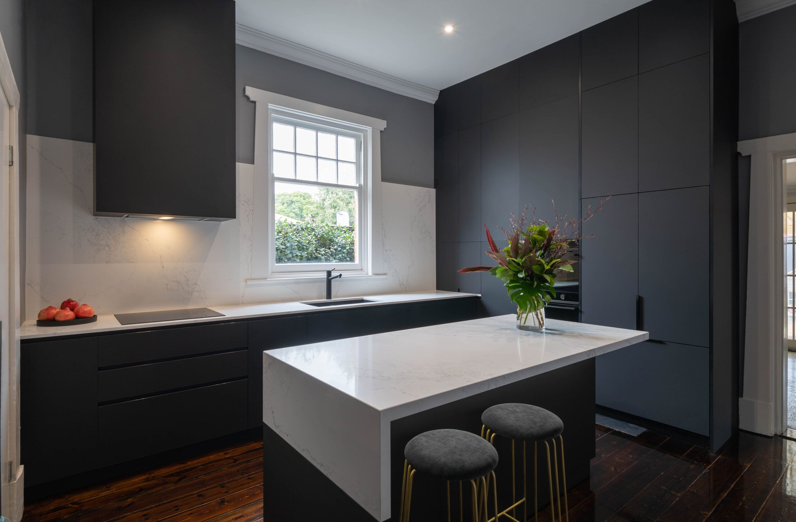 Dark and dramatic Kitchen. Black touch cabinetry with a white marble style benchtop on the island and the back run of cooking space. Large window letting in light and space. Sleek and modern.