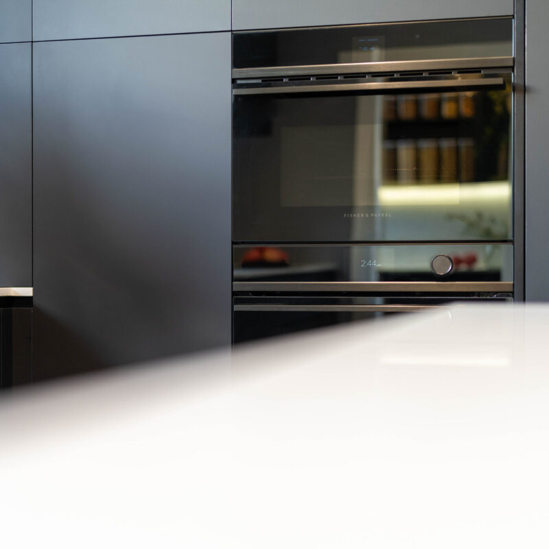 Fisher and Paykel wall ovens surrounded by black touch cabinetry with a white stone benchtop.