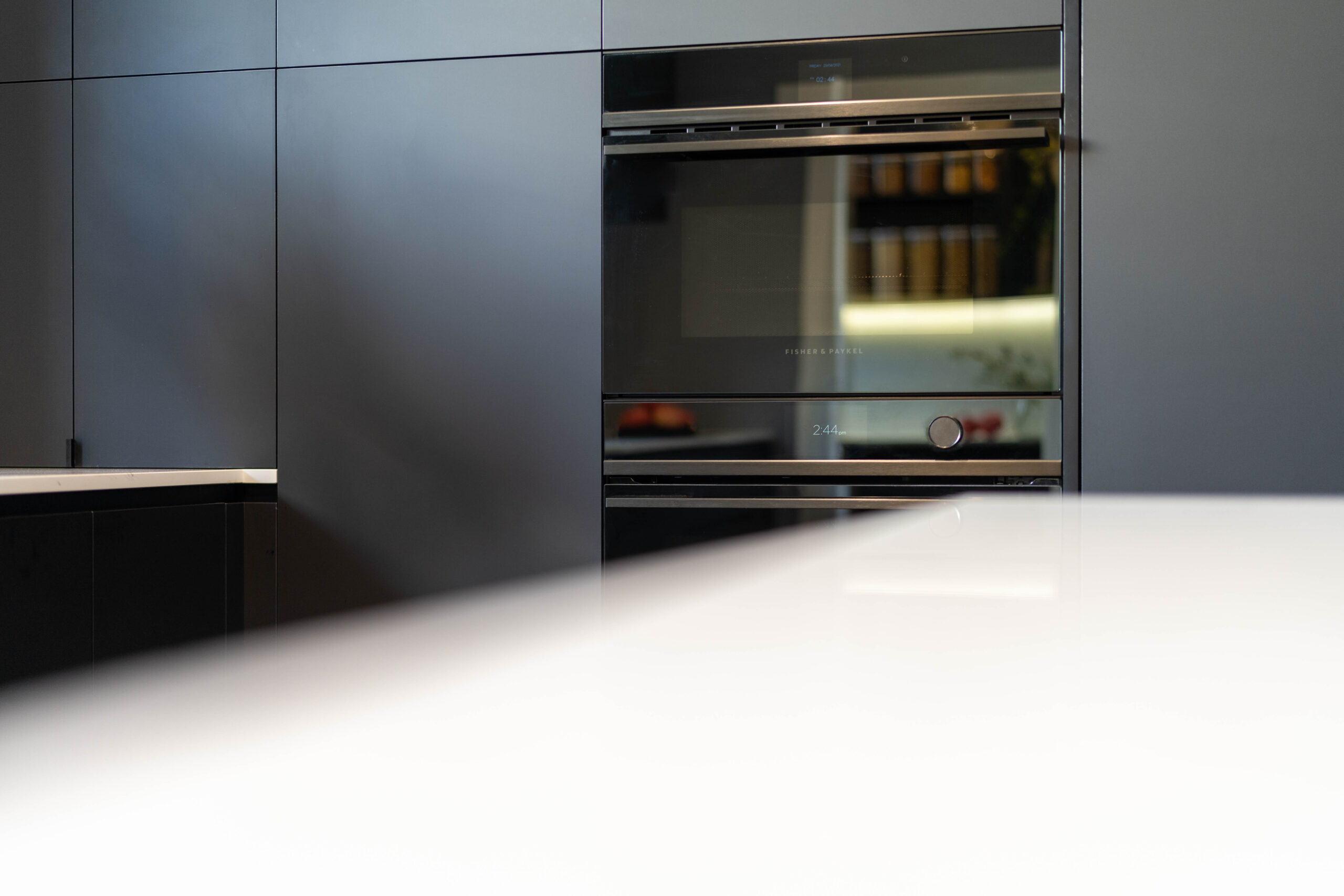 Fisher and Paykel wall ovens surrounded by black touch cabinetry with a white stone benchtop.