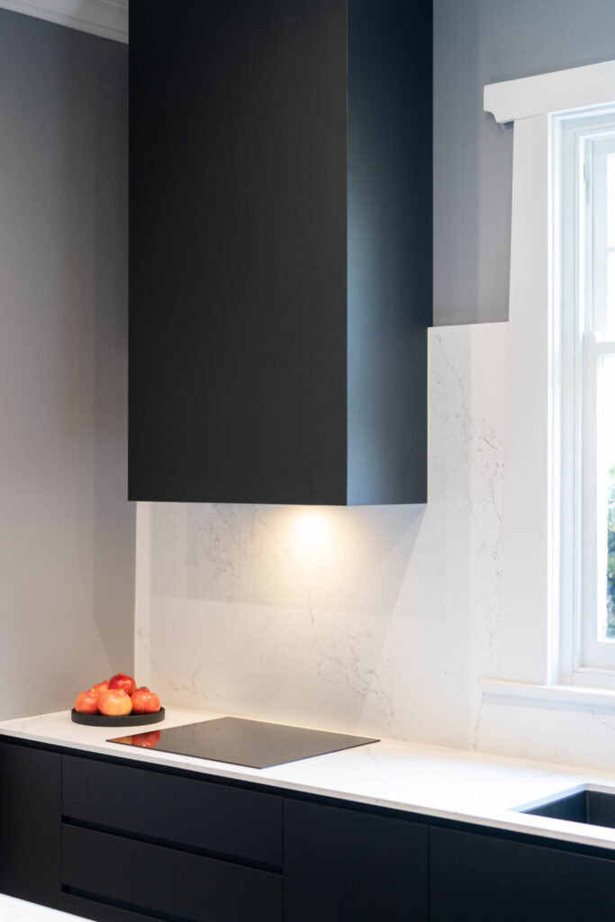 Covered black range hood space with grey walls and marble look stone splashback and benchtop with a flat electric cooktop. Black, white and grey highlights.