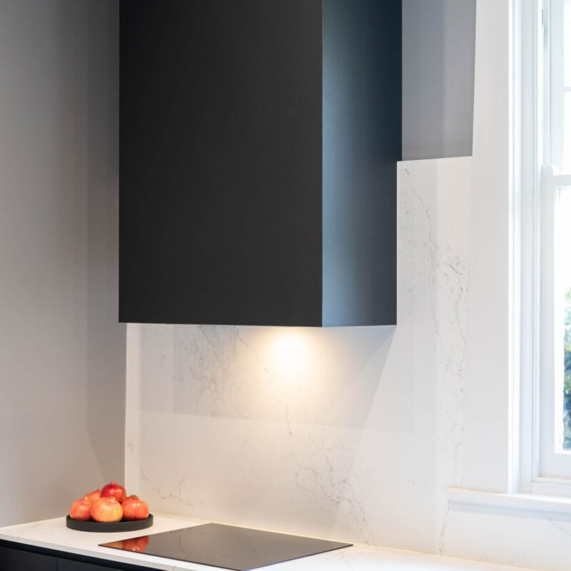 Covered black range hood space with grey walls and marble look stone splashback and benchtop with a flat electric cooktop. Black, white and grey highlights.