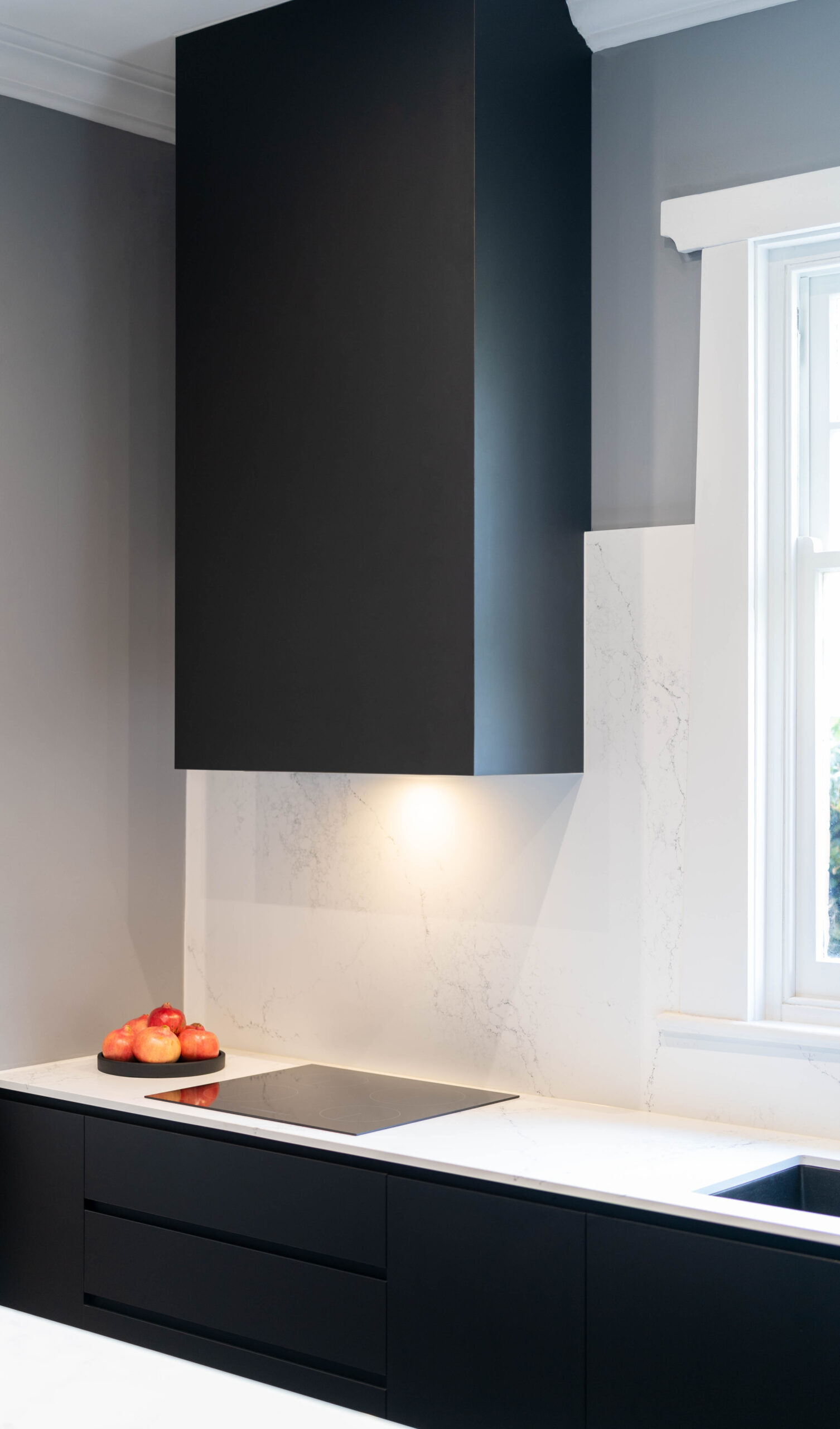 Covered black range hood space with grey walls and marble look stone splashback and benchtop with a flat electric cooktop. Black, white and grey highlights.