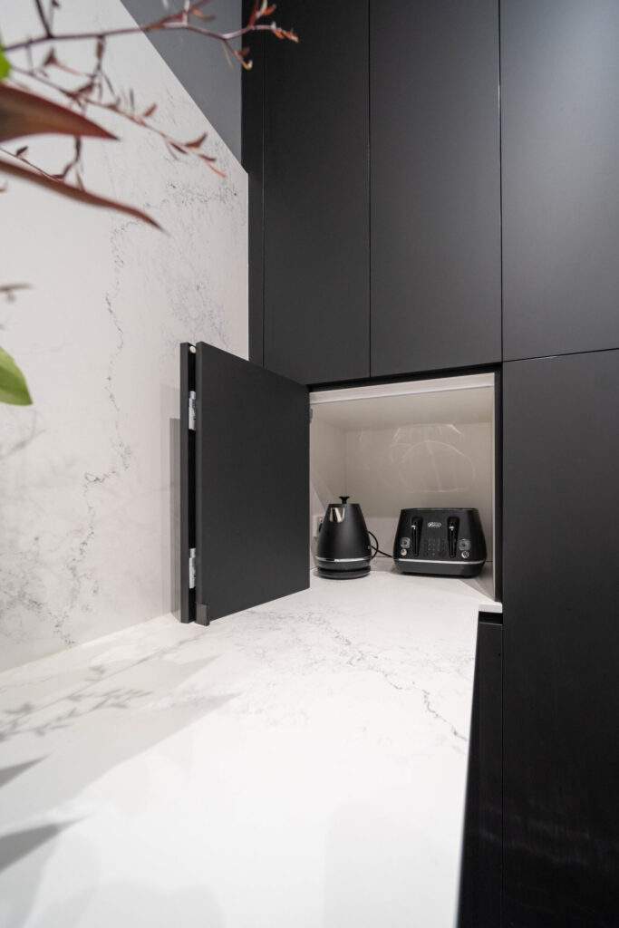 Dark and Dramatic. Kitchen with Black touch hidden nook for small appliances on a white stone marble look benchtop.