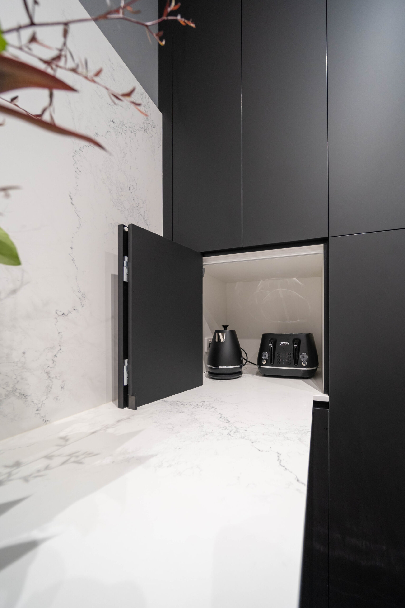 Dark and Dramatic. Kitchen with Black touch hidden nook for small appliances on a white stone marble look benchtop.