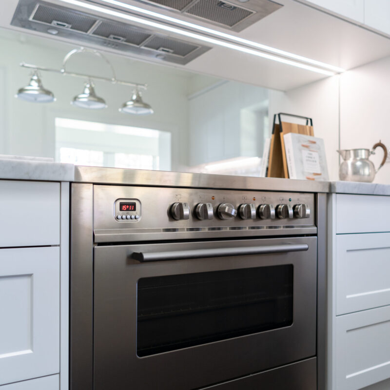 Freestanding Oven in stainless steel highlights the back run of cooking space against a mirrored splashback and white cabinetry and undermount rangehood.