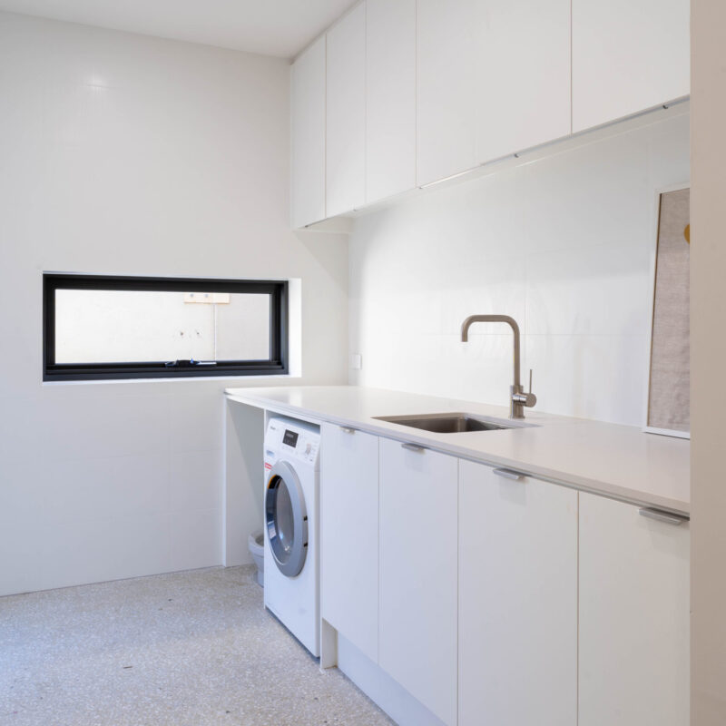 The laundry space is open, clean and light and very modern. A straight line of white cabinetry, floor to ceiling.