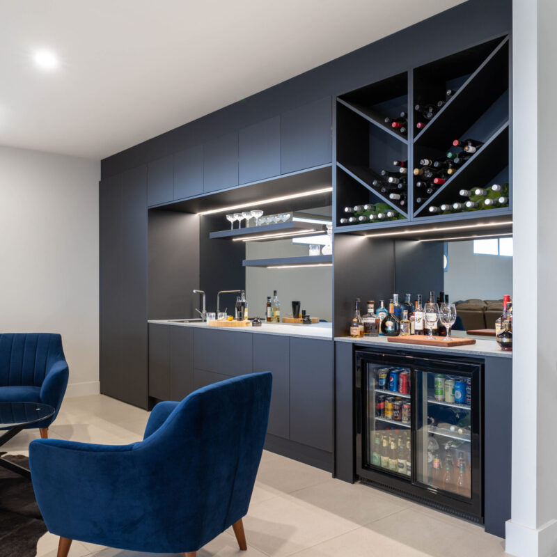 Modern home bar for entertaining. Clean simple lines in Touch supermatte black cabinetry. Mirrored, with shelves and led lights, wine racks, fridge and sink and taps.
