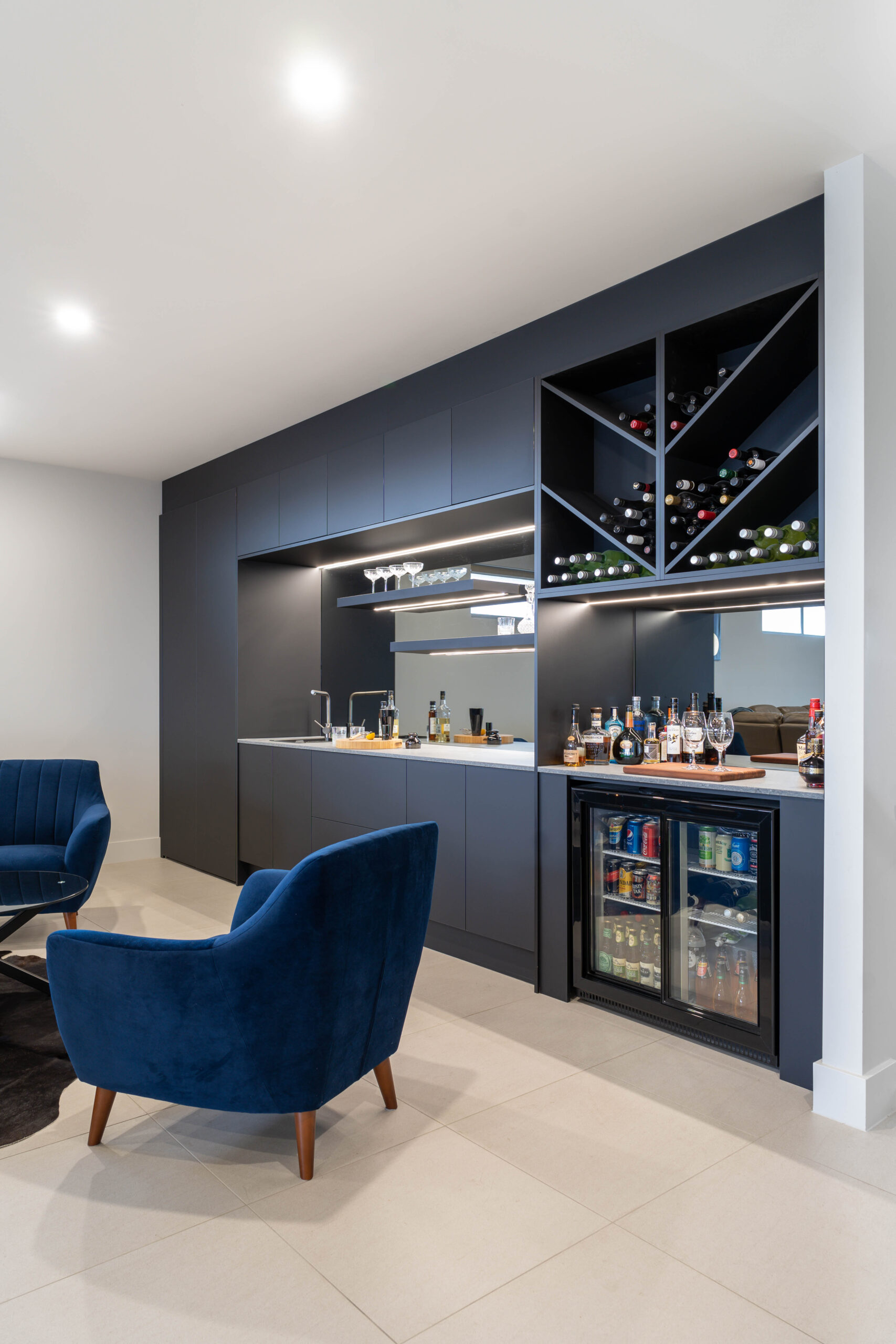 Modern home bar for entertaining. Clean simple lines in Touch supermatte black cabinetry. Mirrored, with shelves and led lights, wine racks, fridge and sink and taps.