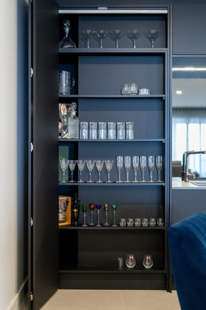 A modern home bar with black cabinet space full of shelving for housing glassware.