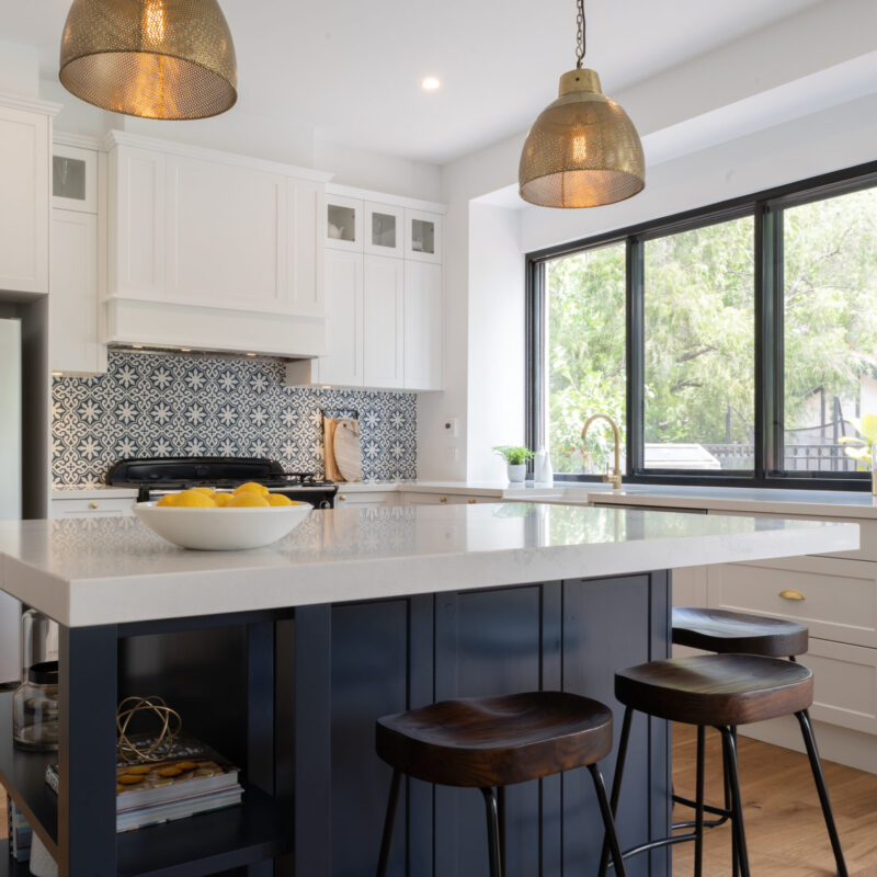 A traditional kitchen in Navy, white and gold. A navy island bench for entertaining and blue and white patterned splashback tiles and a feature.