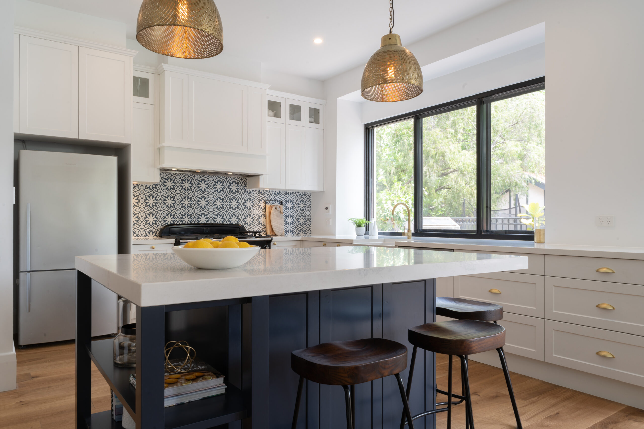 A traditional kitchen in Navy, white and gold. A navy island bench for entertaining and blue and white patterned splashback tiles and a feature.