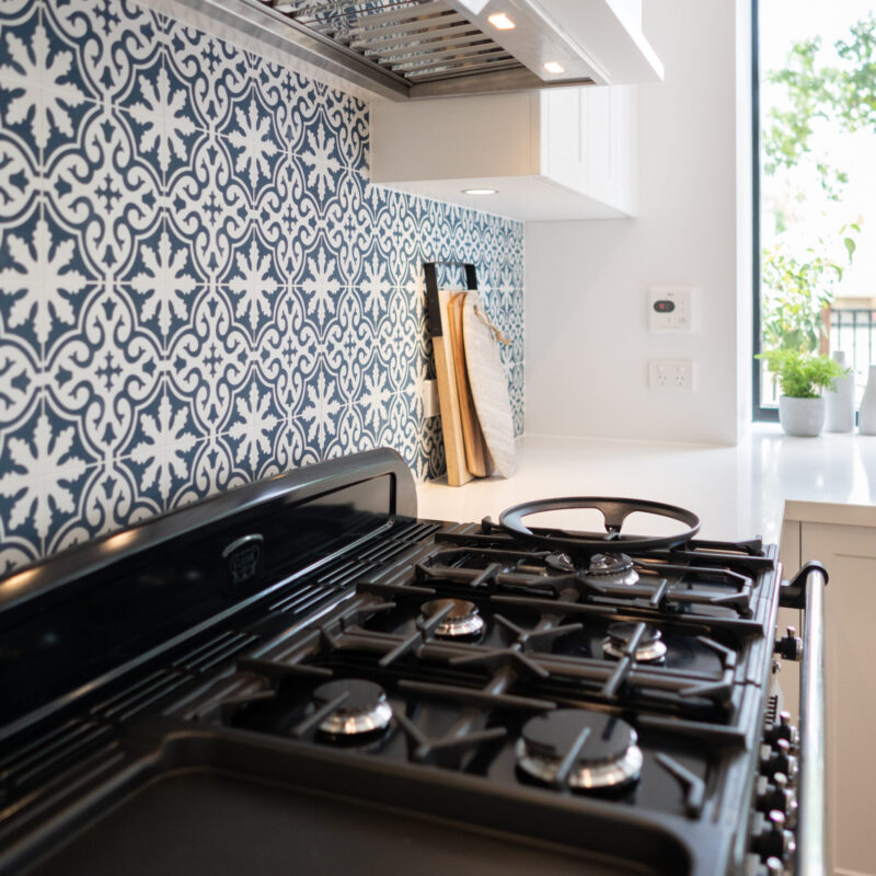 Cooking space with blue and white patterned tiles and undermount rangehood, located next to a bright open window.