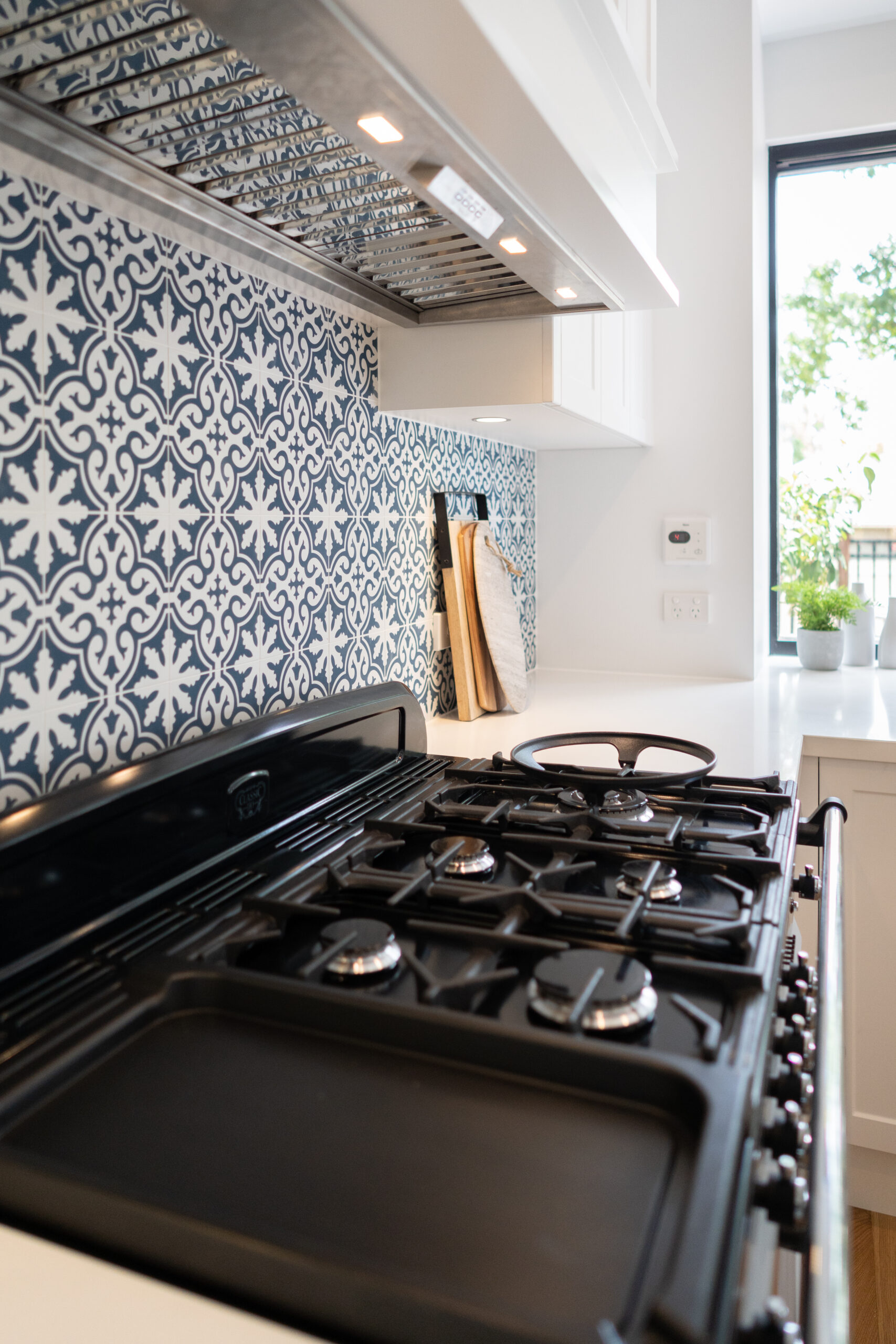 Cooking space with blue and white patterned tiles and undermount rangehood, located next to a bright open window.