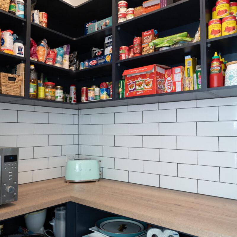 Walk in Pantry. Over head navy open shelving for storage and timber benchtop with open under bench shelving. White gloss subway tiles to match.