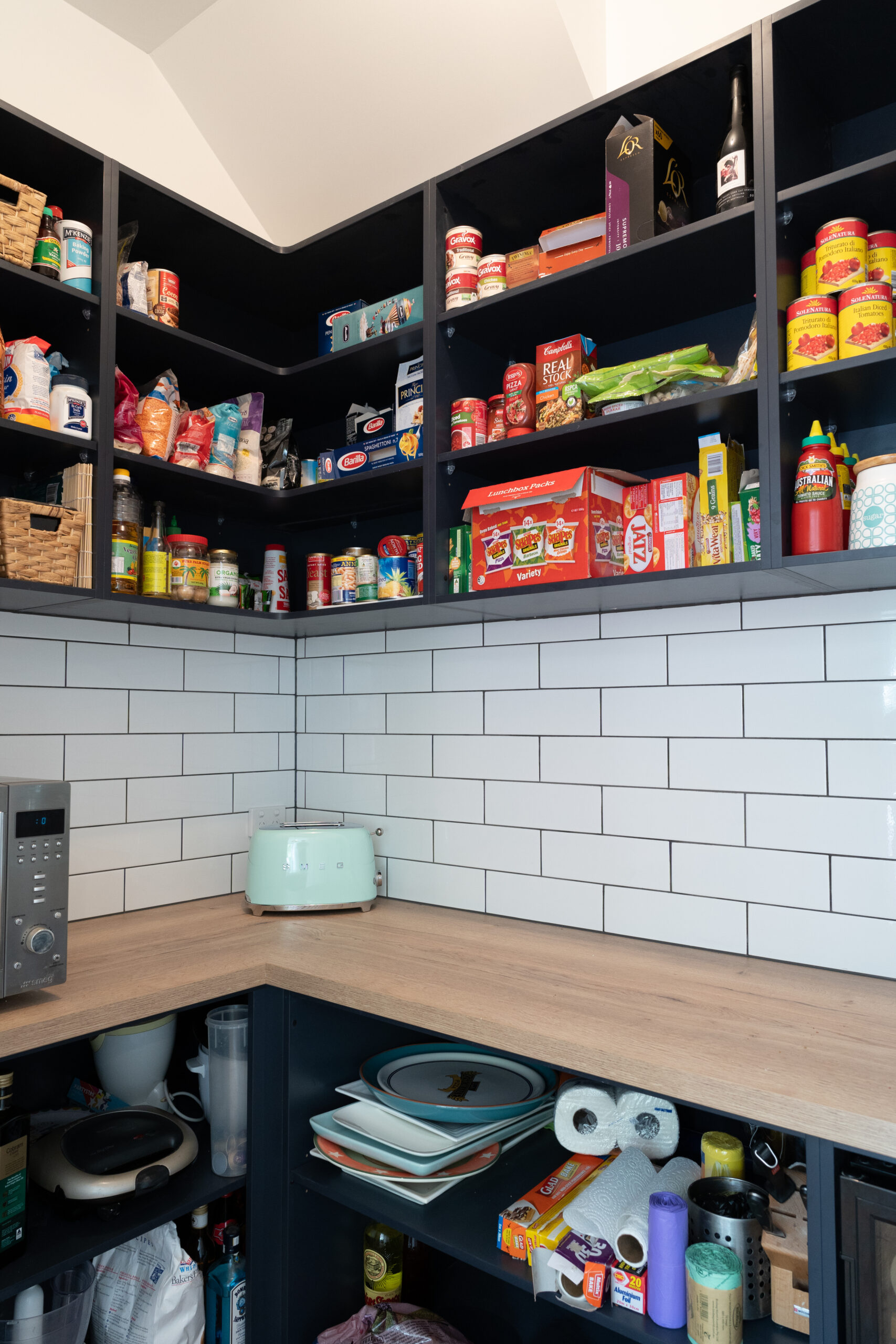 Walk in Pantry. Over head navy open shelving for storage and timber benchtop with open under bench shelving. White gloss subway tiles to match.