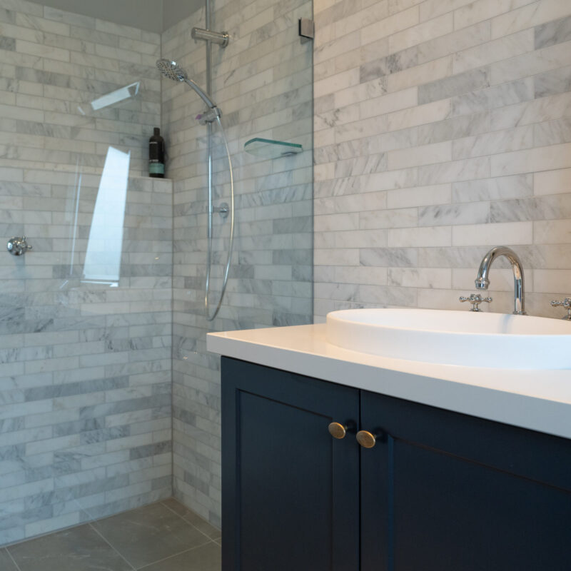 Bathroom space with glass shower and Navy Barossa profile two door vanity unit. White and grey marble look tiles and silver traditional tapware.