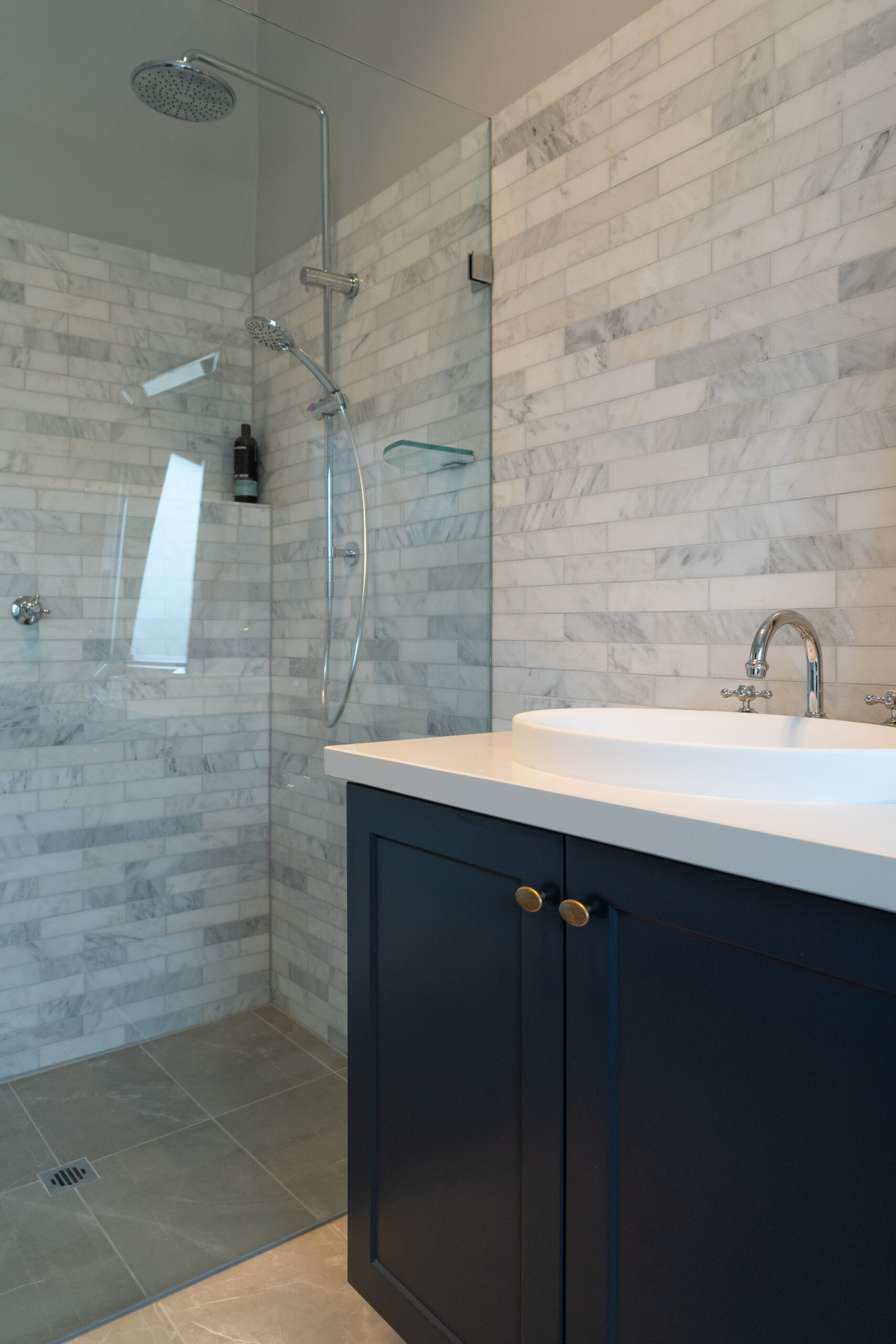 Bathroom space with glass shower and Navy Barossa profile two door vanity unit. White and grey marble look tiles and silver traditional tapware.