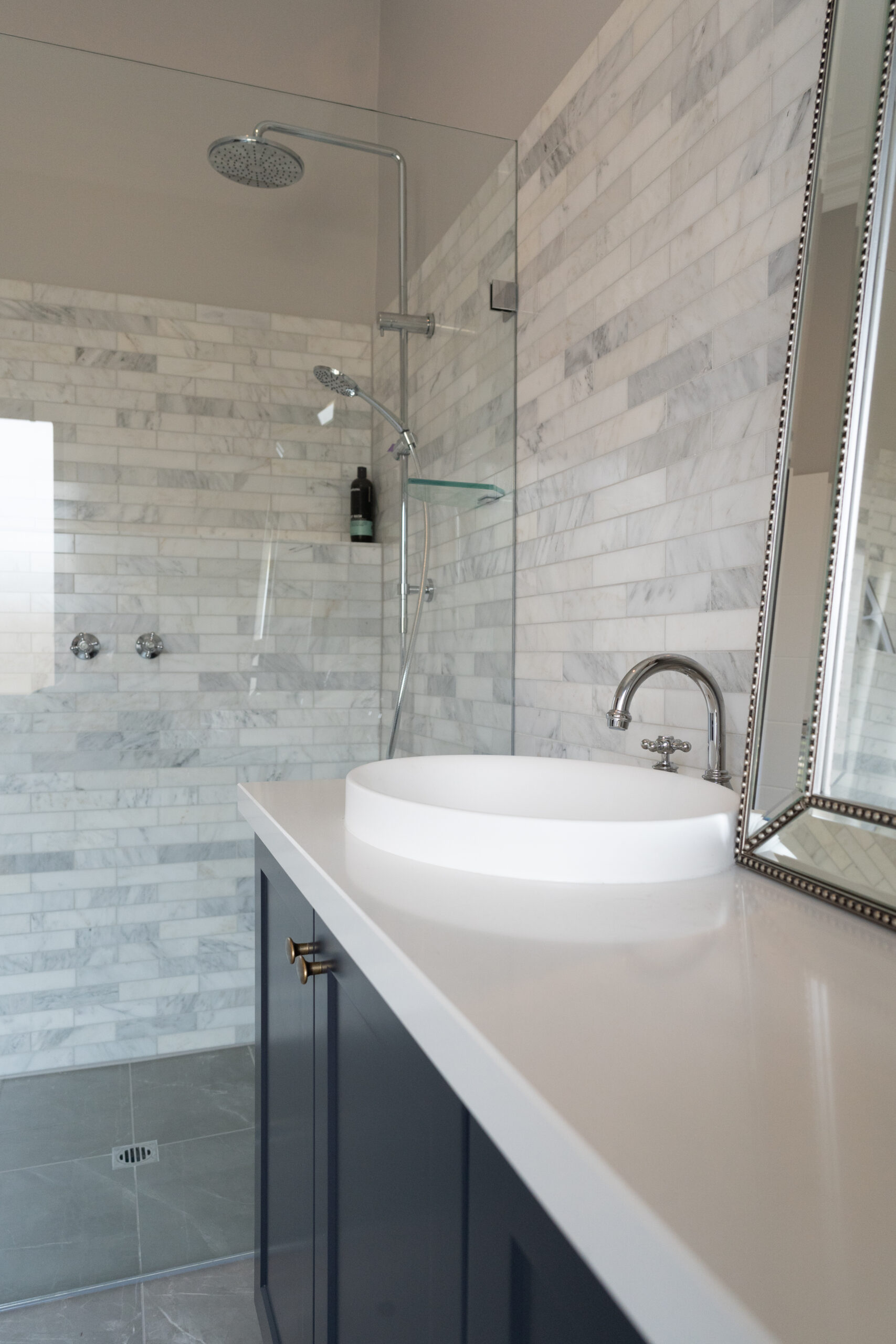 Bathroom space with glass shower and Navy Barossa profile two door vanity unit. White and grey marble look tiles and silver traditional tapware.