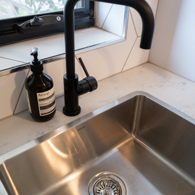 Laundry tub, black tapware and large herringbone gloss tiles.