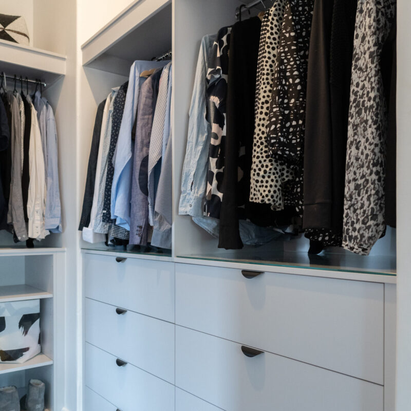 Walk in robe storage and hanging space. White Grey cabinetry and black cup handles and glass shelving.