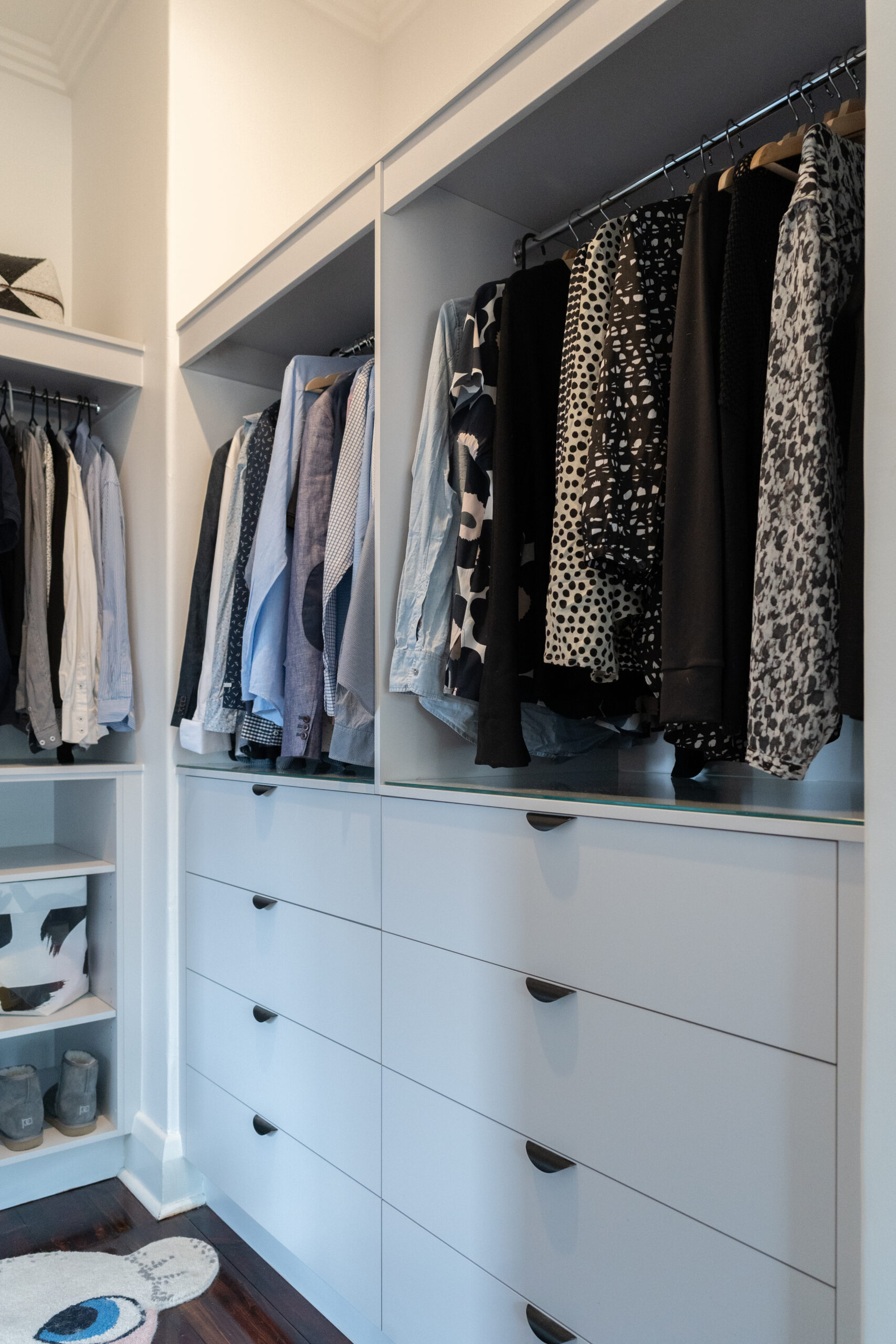 Walk in robe storage and hanging space. White Grey cabinetry and black cup handles and glass shelving.