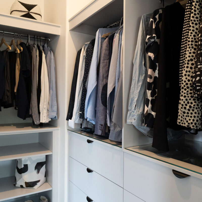 Walk in robe storage and hanging space. White Grey cabinetry and black cup handles and glass shelving.