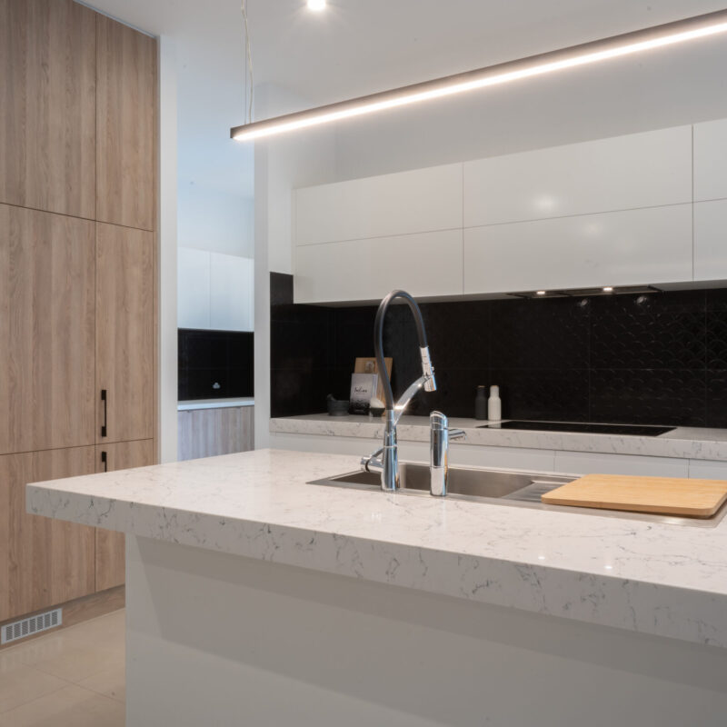 A modern masterpiece kitchen. Thick stone benchtops in grey tones with black, white and timber features. Large island with integrated dishwasher and large sink and tap.