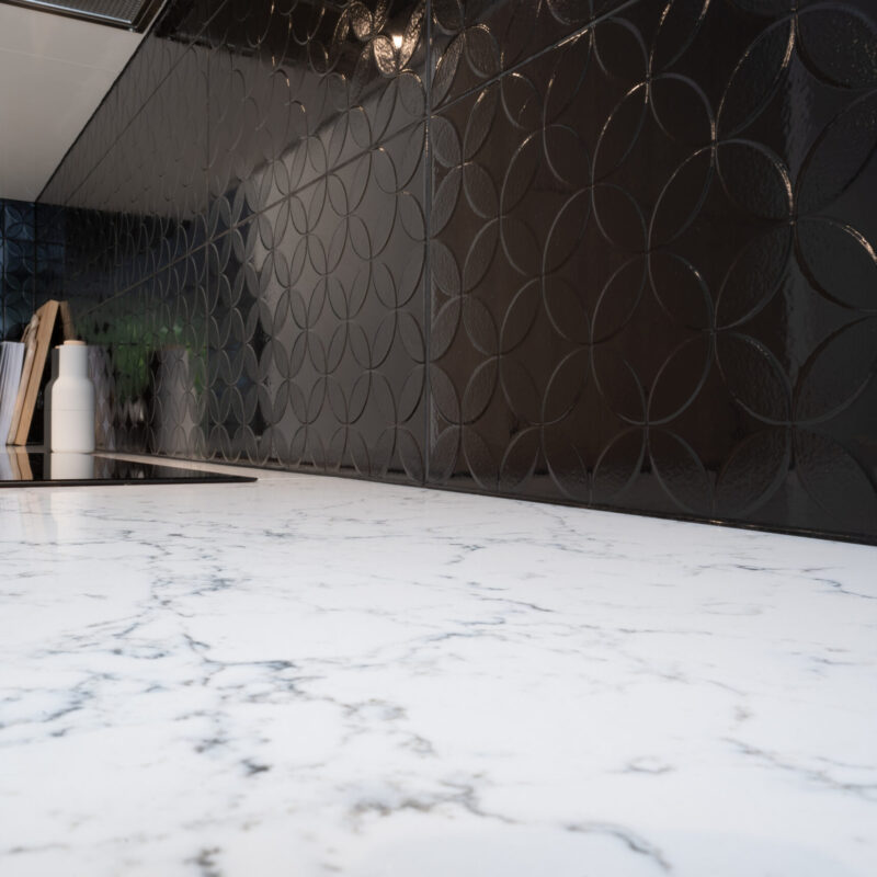 Cooking space with grey tones stone benchtop and black patterned gloss tiled Splashbacks.