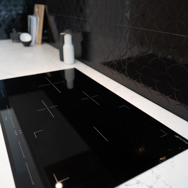 Kitchen cooking space with electric cooktop against the black splashback and white grey stone benchtop.