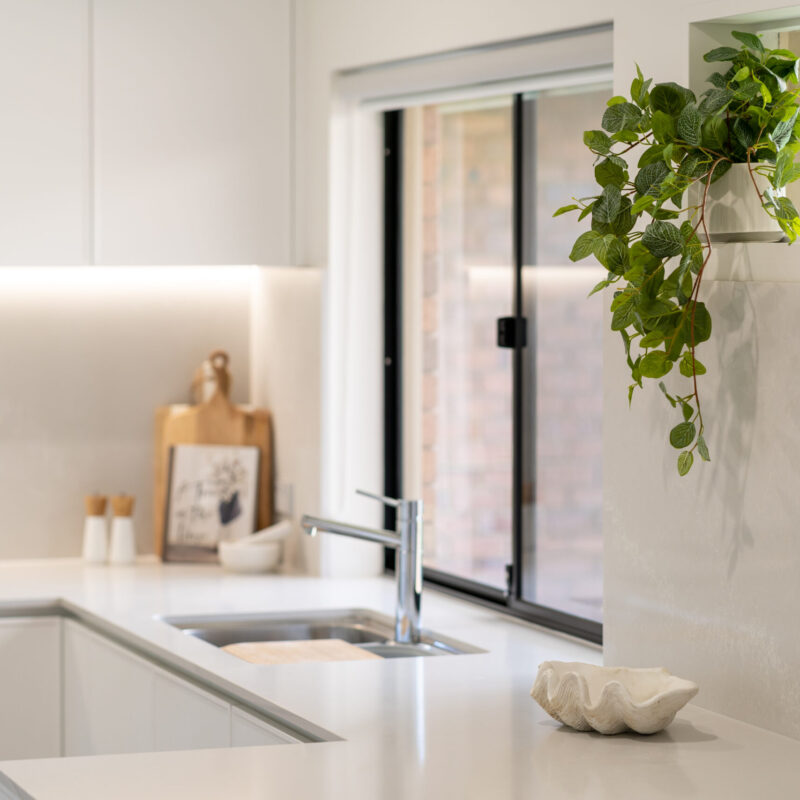 White simple Kitchen. Light and fresh. Silver sink and taps and large window.