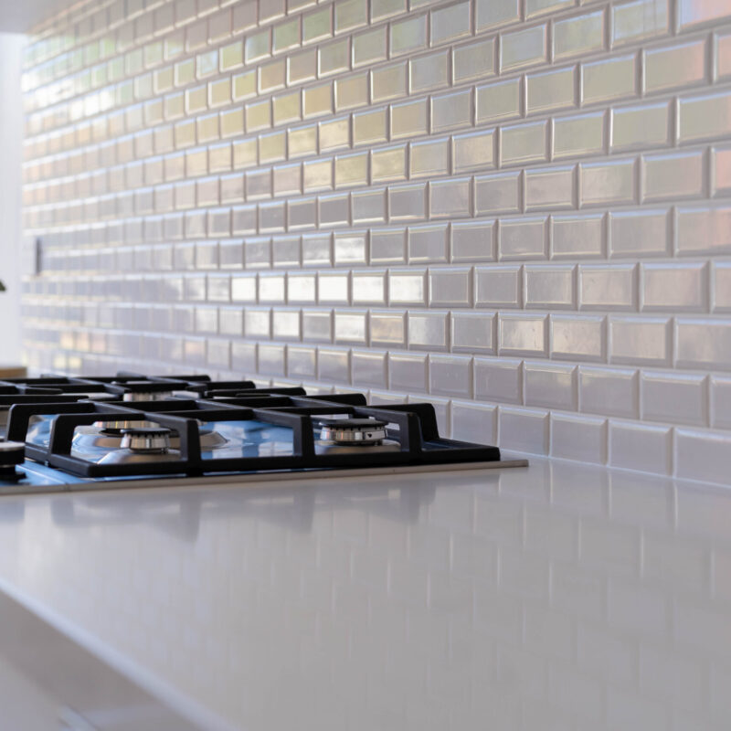 White gloss subway splashback with gas cooktop, reflected by the light of the large window.