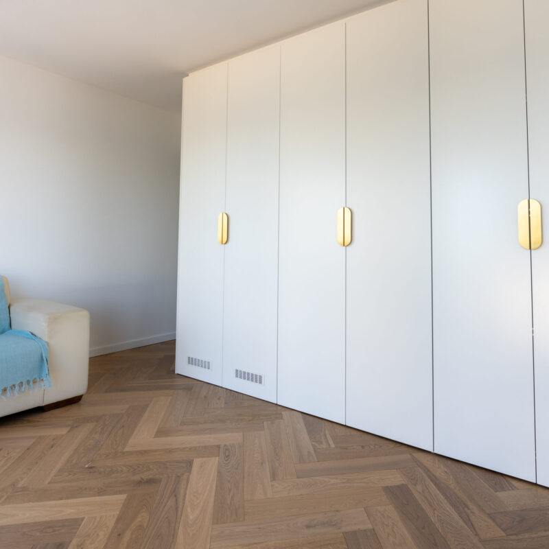Light and bright full height cabinets concealing a kitchenette behind. White cabinets with brushed gold handles.