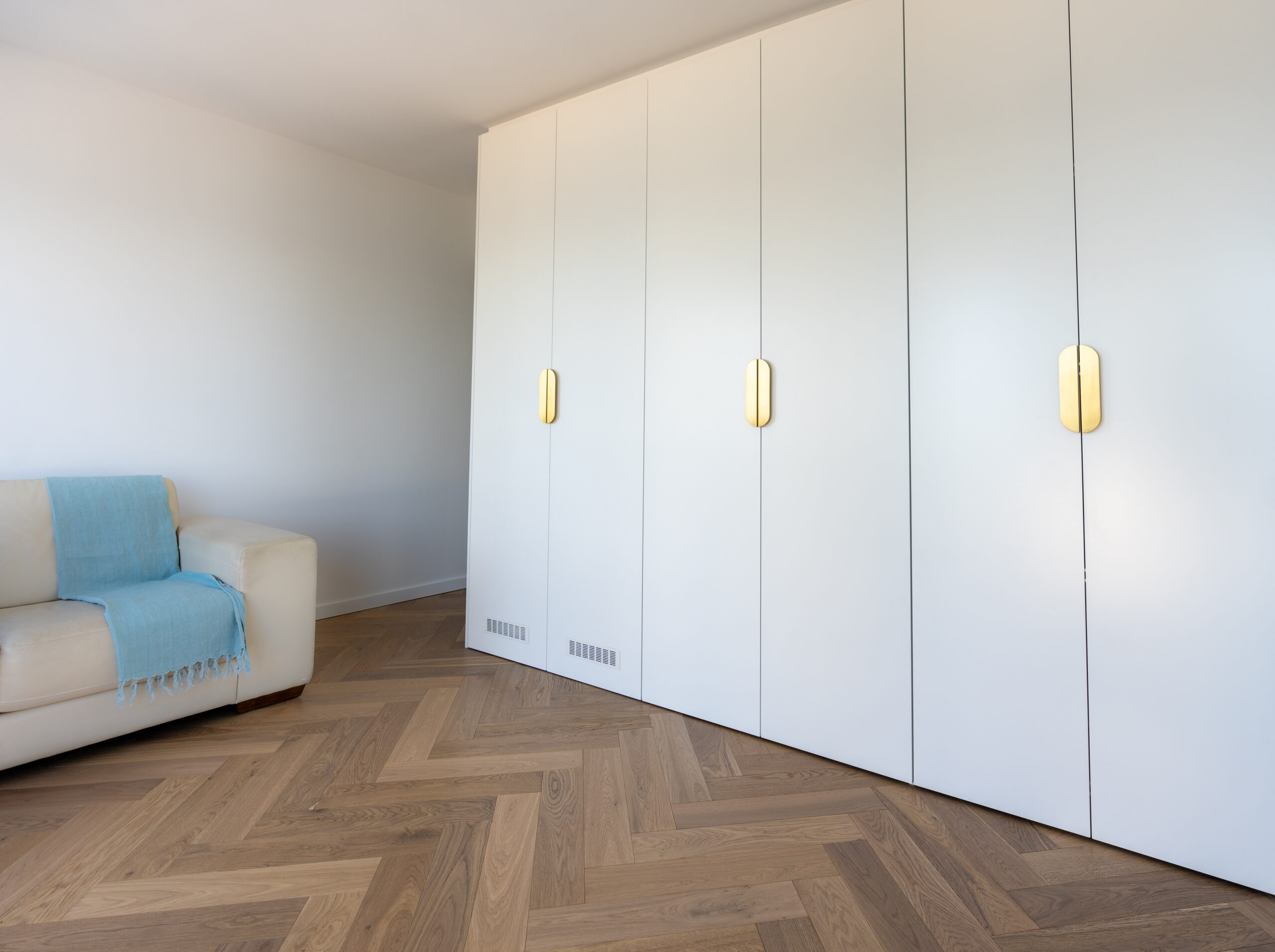 Light and bright full height cabinets concealing a kitchenette behind. White cabinets with brushed gold handles.