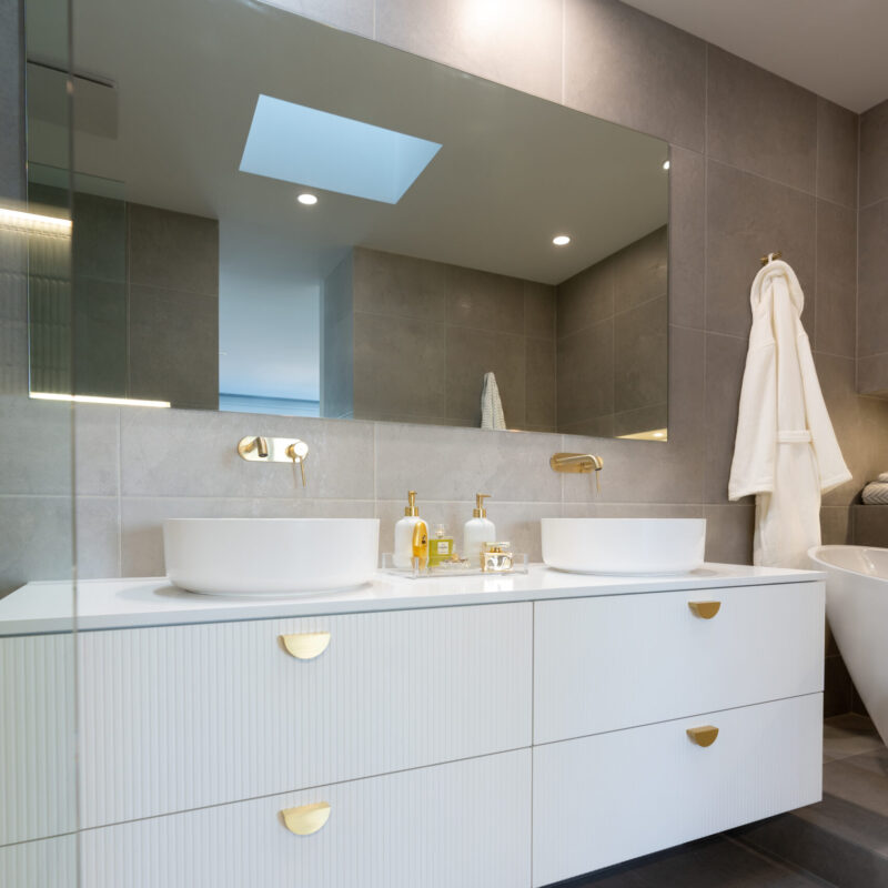 Double vanity. White floating cabinets in Metz profile with brushed gold handles. White stone benchtop with counter top basins.