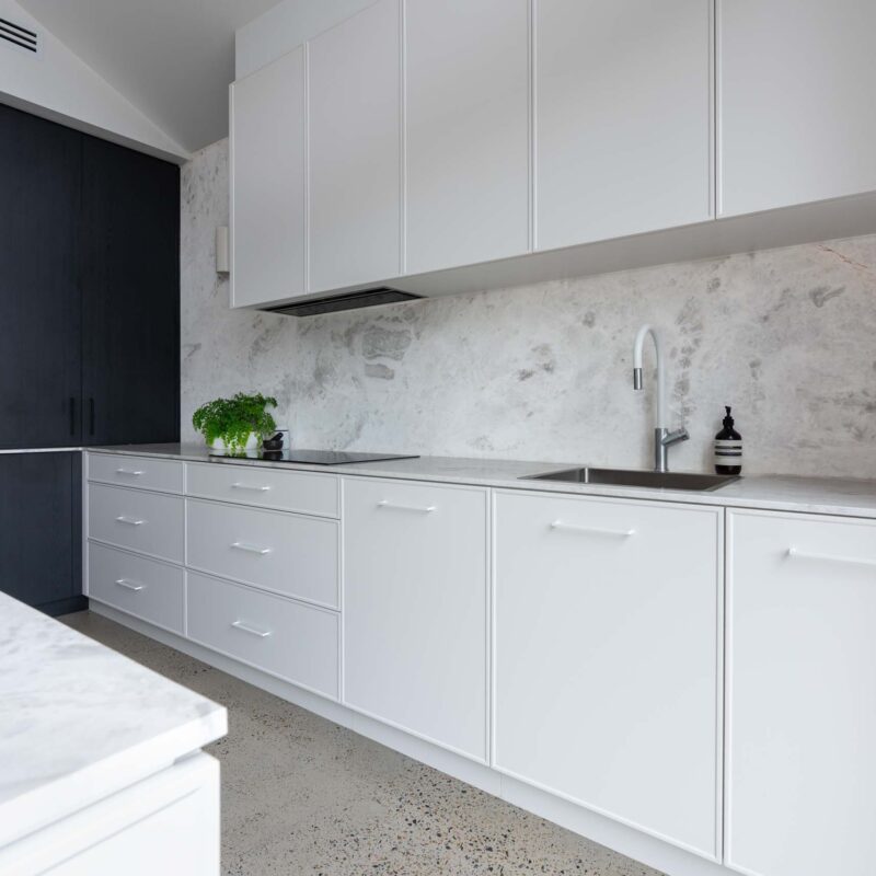 Slim shaker style profiled white cabinets. Matte white handles. Featuring a marble splashback with white overhead cabinets.