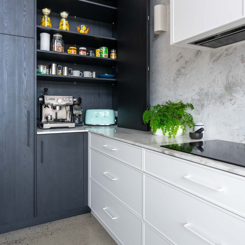 Black wood grain cabinets with sliding doors concealing a coffee nook / pantry behind. Featuring light marble benchtop and splashback.