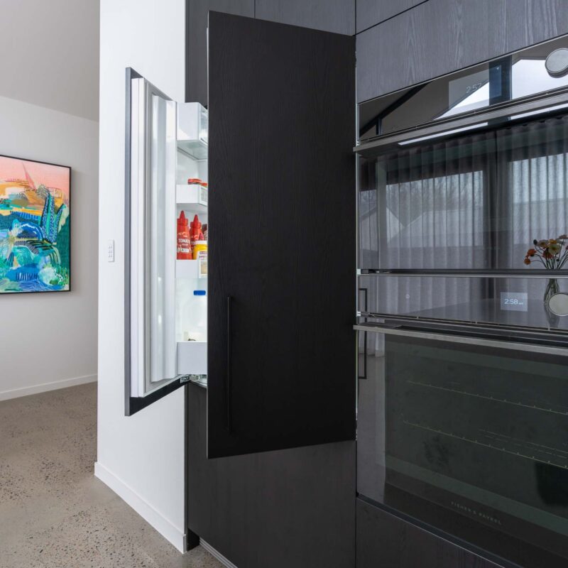 Black wood grain floor to ceiling cabinet. Featuring a hidden integrated double door fridge, and built in ovens.