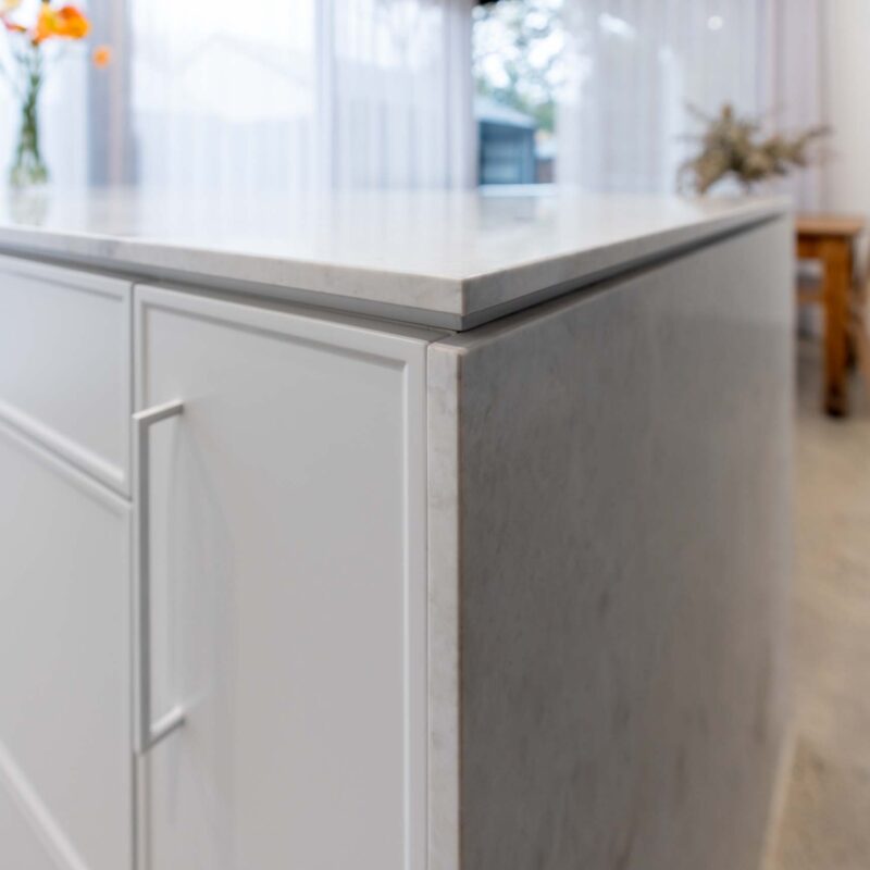 Light marble island benchtop with white slim shaker-style doors and drawers