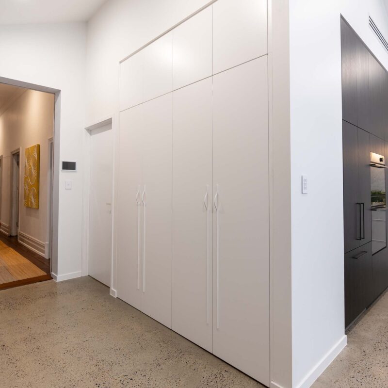 Floor-to-ceiling matte white cabinetry with matching matte white handles concealing a hidden laundry.