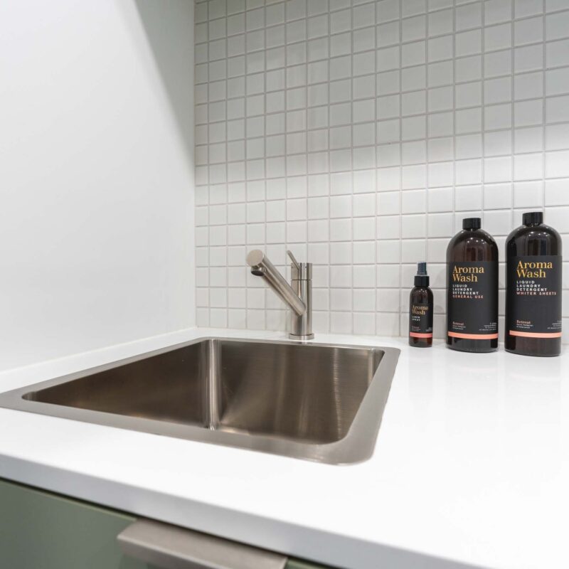 Top-mount stainless steel sink with matching tap, set against a white small square tile splashback.