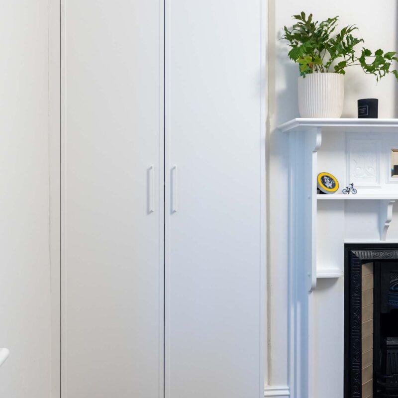 Bedroom with central fire place and floor to ceiling wardrobes either side. Featuring white slim shaker style doors.