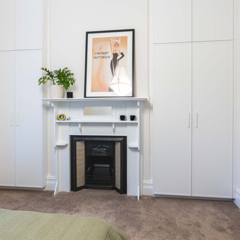Bedroom with central fire place and floor to ceiling wardrobes either side. Featuring white slim shaker style doors.