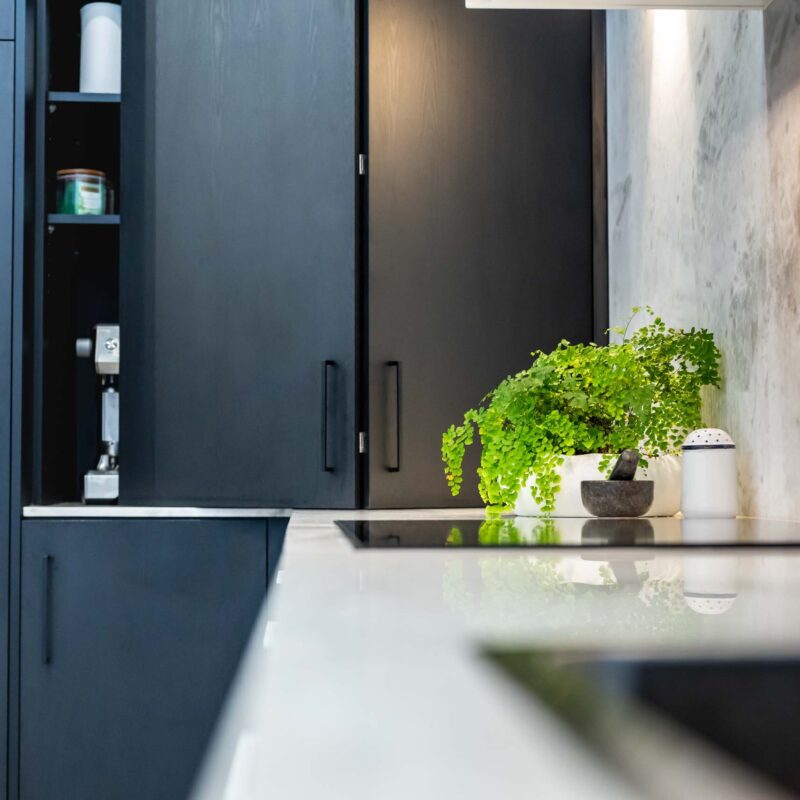 Black wood grain cabinets with sliding doors concealing a coffee nook / pantry behind. Featuring grey marble benchtop and splashback.
