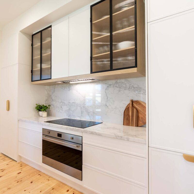 White kitchen featuring white slim shaker profile doors and drawers and light marble benchtops. Glass fluted overhead cabinets.