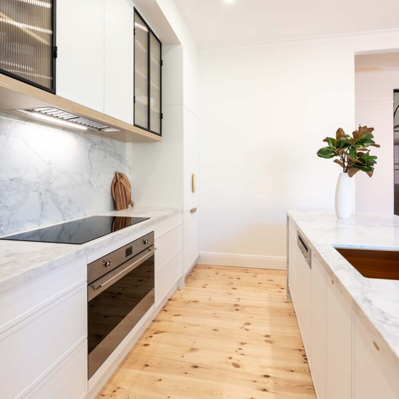 White galley style kitchen featuring white slim shaker profile doors and drawers and light marble benchtops. Glass fluted overhead cabinets.