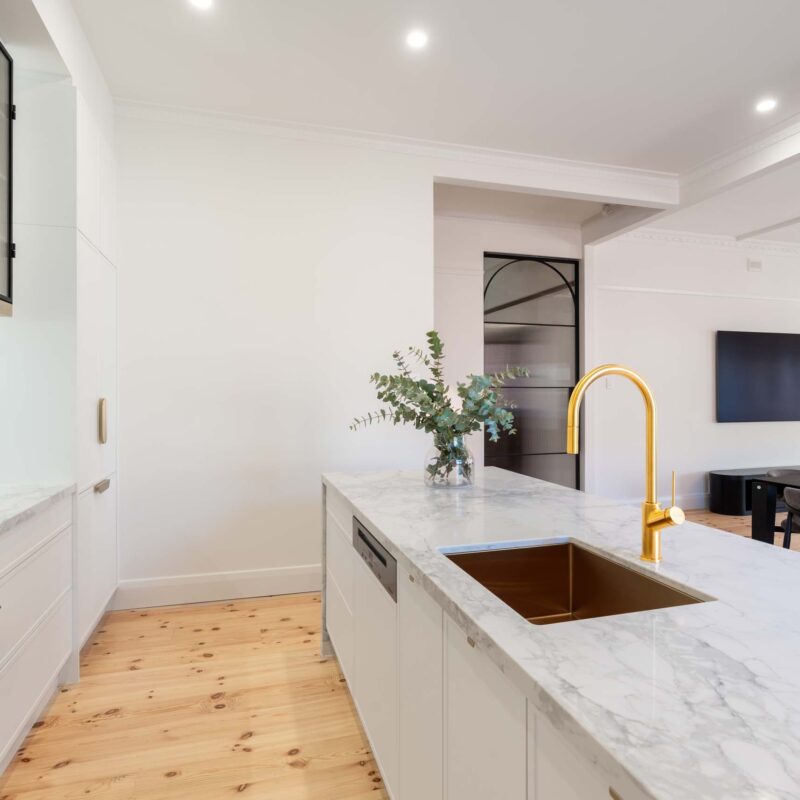 White galley style kitchen featuring white slim shaker profile doors and drawers and light marble benchtops. Glass fluted overhead cabinets.