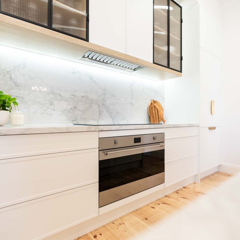 White kitchen featuring white slim shaker profile doors and drawers and light marble benchtops. Glass fluted overhead cabinets.