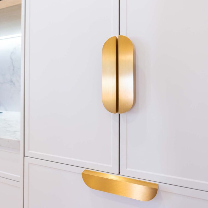 White slim shaker-profile doors concealing a fridge-freezer, finished with matte gold handles.