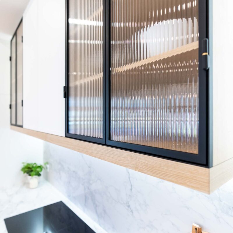 Overhead cabinets with fluted glass doors. Light marble benchtop with induction cooktop below.